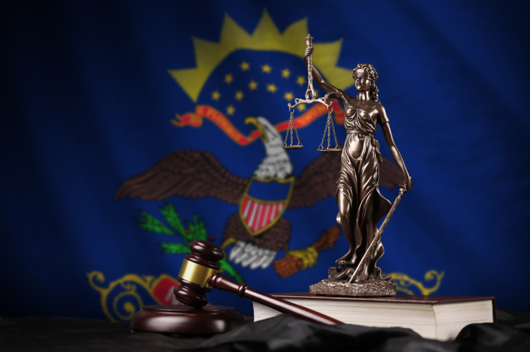 A judge's gavel and a statue of Lady Justice infront of the flag of North Dakota (© Shutterstock/Mehaniq)
