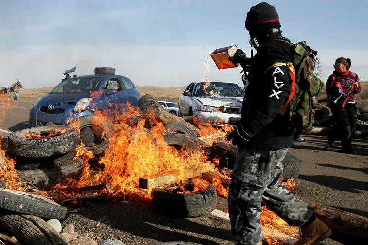 A protester pours gasoline on a fire blocking North Dakota Highway 1806 on Oct. 27, 2016, north of Cannon Ball. Protesters of the Dakota Access Pipeline were attempting to keep law enforcement officers from pushing them off the road and out of their camp. (copyright by INFORUM)